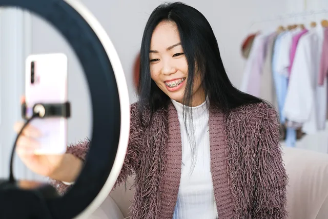 Smiling woman using smartphone and ring light for live streaming indoors. Micro influencer marketing advertising rules: paid-promotion labels, children's data and the £1,000 trading allowance