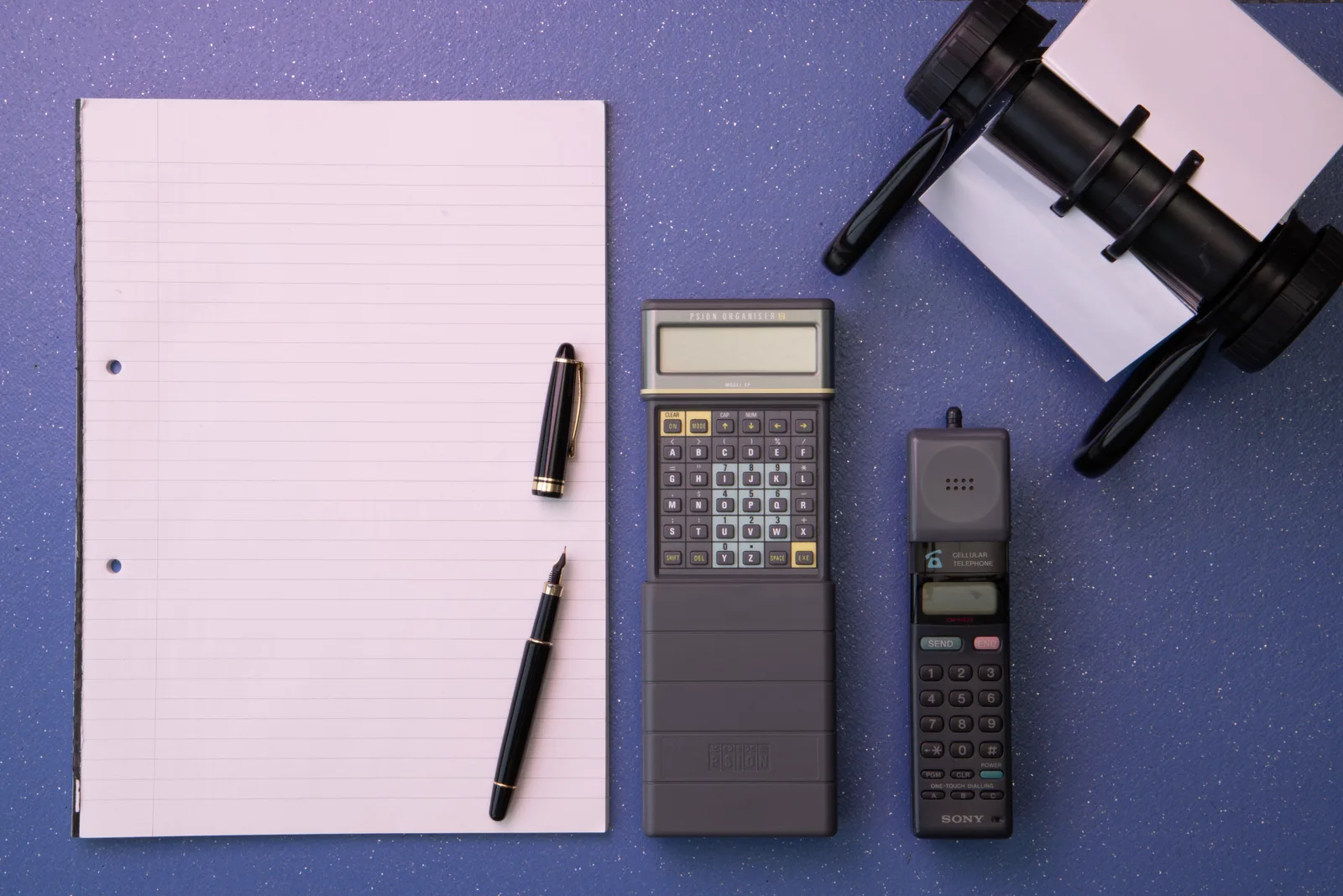 Flat lay of vintage office items including a calculator, mobile phone, and paper on a blue background.