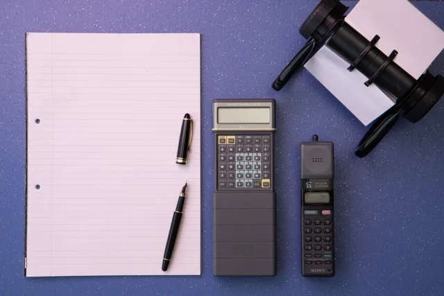 Flat lay of vintage office items including a calculator, mobile phone, and paper on a blue background. Micro-influencer marketing operating workflow for paying creators: status check, VAT invoice and payment date